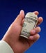 Roll of $100 bills gripped in a person's hand, in front of a deep blue background