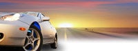 A silver car driving down the road with a bright sunset in the background