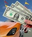 Hand holding $1 bills with orange car in the background and flags