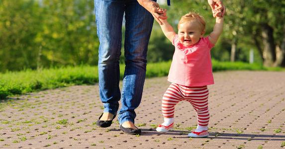 Baby taking her first steps with mother holding hands | NadyaEugene/Shutterstock.com