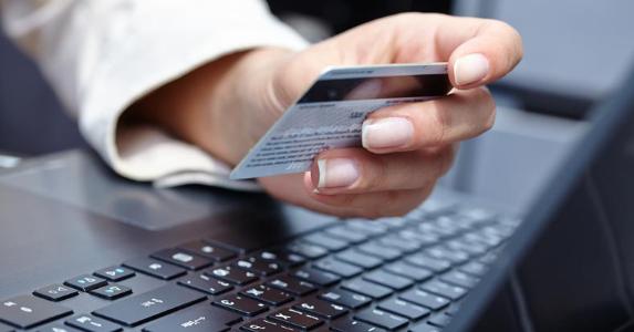 Close-up of woman holding credit card near laptop © Denis Vrublevski/Shutterstock.com