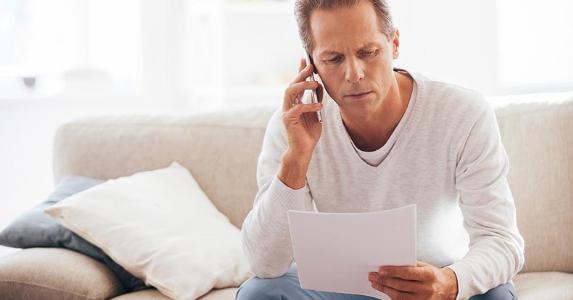 Concerned man calling adviser, looking at papers © iStock