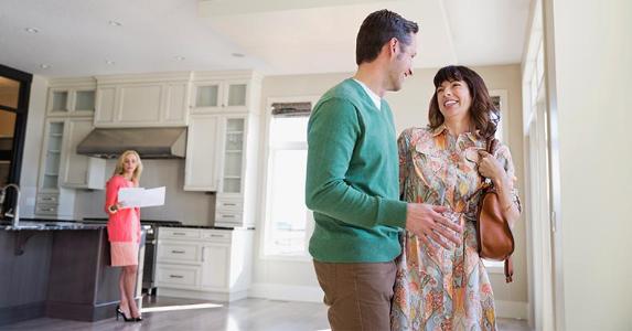 Tips for buying a home in foreclosure Couple discussing potential house purchase with agent on background | Hero Images/Getty Images