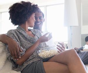 Couple laughing and eating popcorn on the couch | David Jakle/Image Source/Getty Images