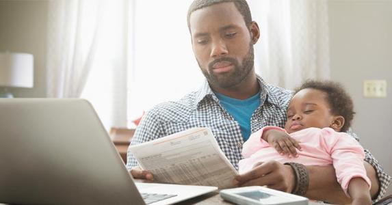 Be on the lookout for personal loan fees Dad reading bill while holding baby | KidStock/Getty Images