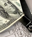 A one hundred dollar bill being cut in half and paperwork in the background