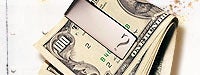 A roll of money with a 100 dollar bill on top with a money clip with a t "?" on it and a dirty white background