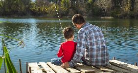 Father sitting on a dock with his son fishing © Nikola Solev/Shutterstock.com