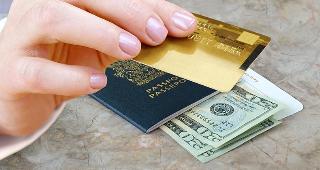 Hand holding credit card with passport and money on desk © NAN728/Shutterstock.com