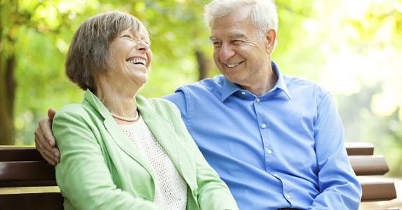 Reverse mortgage fees to buy home worry seniors Laughing senior couple sitting on bench outdoors | alvarez/Vetta/Getty Images