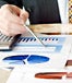 Male hands holding pen over financial charts.