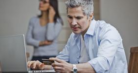 Man at computer holding card wife in background © La India Piaroa/Shutterstock.com