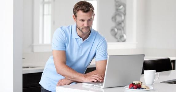 How to protect your online banking transactions Man in blue shirt browsing computer on breakfast counter | iStock.com/BrittaKokemor