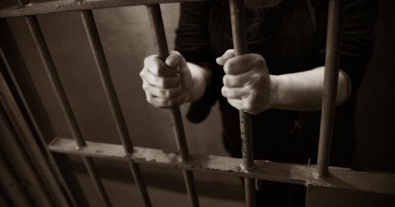 Man in jail cell holding bars © iStock