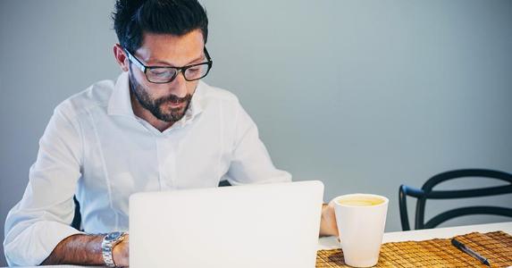 3 steps in deciding how much car you can afford Man in white shirt browsing laptop and drinking coffee | deimagine/Getty Images