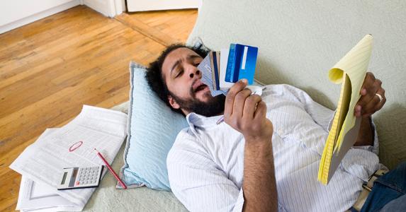 Man laying on the couch looking at his credit cards © iStock
