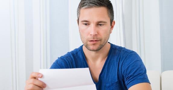 Man unhappily looking at a piece of paper © iStock