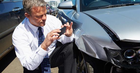 Man taking picture of totaled car © Monkey Business Images/Shutterstock.com