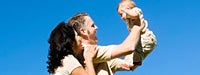 A man holding up a small baby with his wife hugging his shoulder and looking at the baby