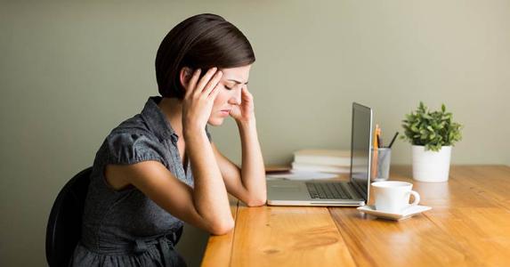 Stressed woman with a headache in home office | iStock.com/Aldo Murillo Stressed woman with a headache in home office | iStock.com/Aldo Murillo