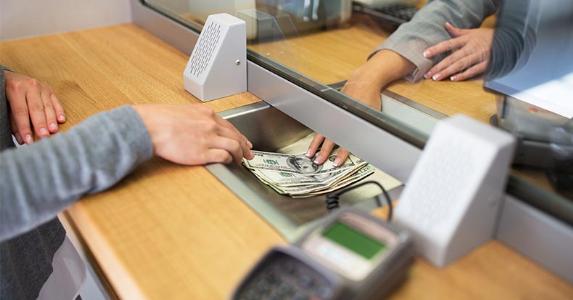 Credit Union Checking Survey Teller passing cash to customer through bank window | Syda Productions/Shutterstock.com