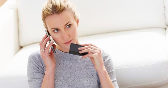 Woman leaning on white sofa holding credit card on the phone © iStock