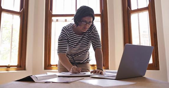 How to defer real estate losses if you earn too much Woman leaning over and writing on paper | PeopleImages/DigitalVision/Getty Images