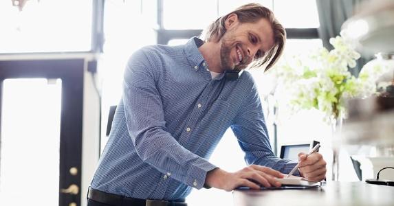 Self-employed and applying for a personal loan Smiling man filling out a book at hotel desk | HeroImages/Hero Images/Getty Images